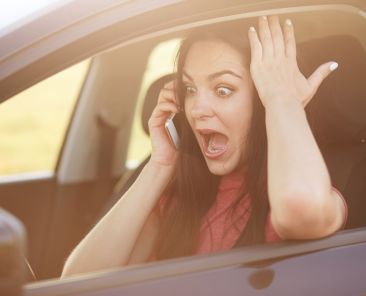 Shocked beautiful young female driver doesnt know how to repair car, makes call to husband via cellular, stares with surprisement and fear, keeps jaw dropped, poses in automobile. Omg concept