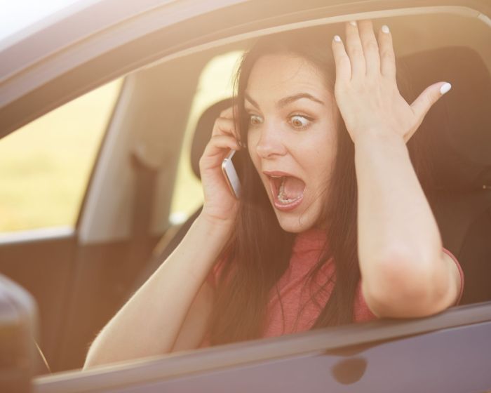 Shocked beautiful young female driver doesnt know how to repair car, makes call to husband via cellular, stares with surprisement and fear, keeps jaw dropped, poses in automobile. Omg concept